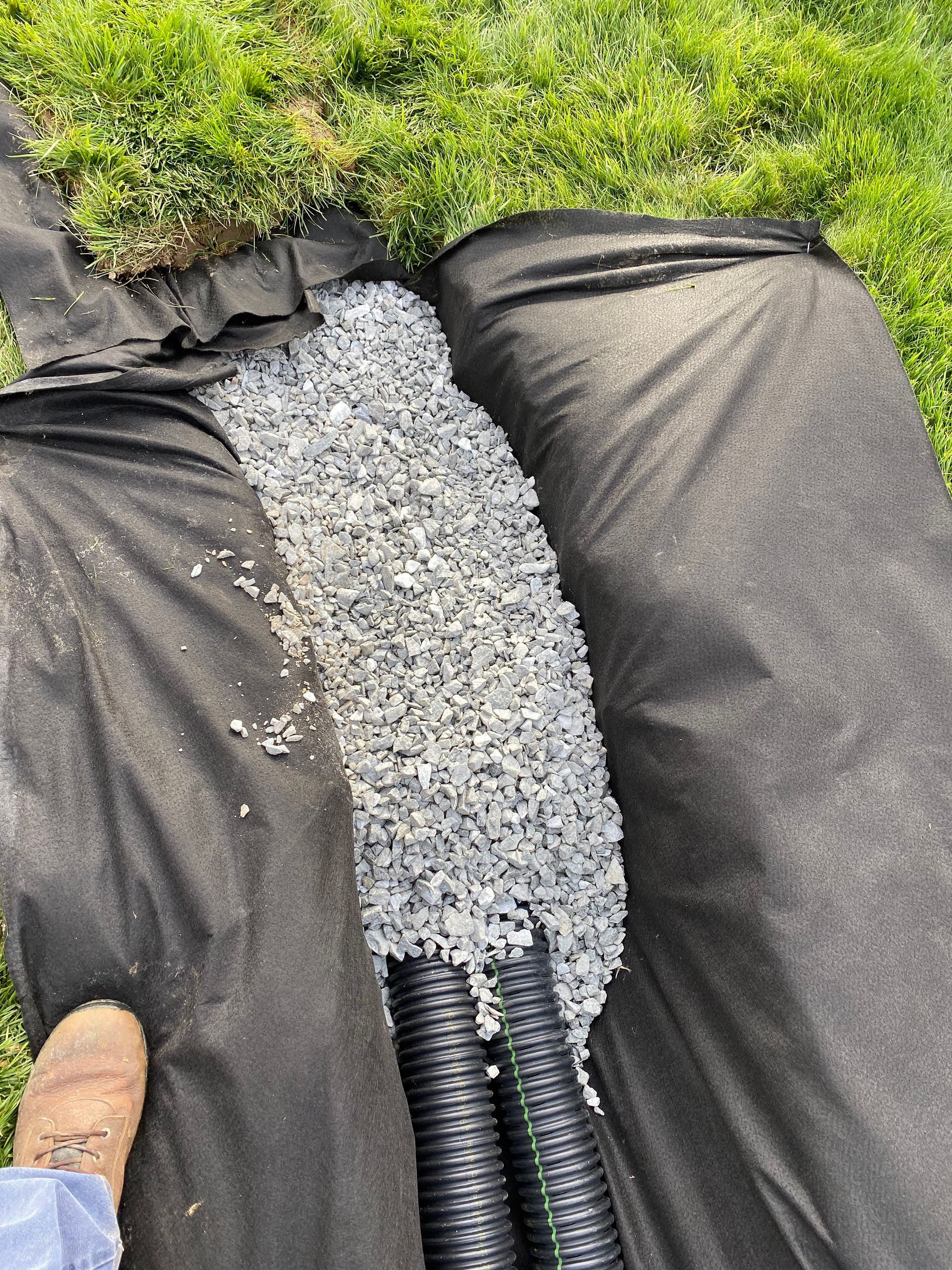 A person is standing next to a pile of gravel and a hose.