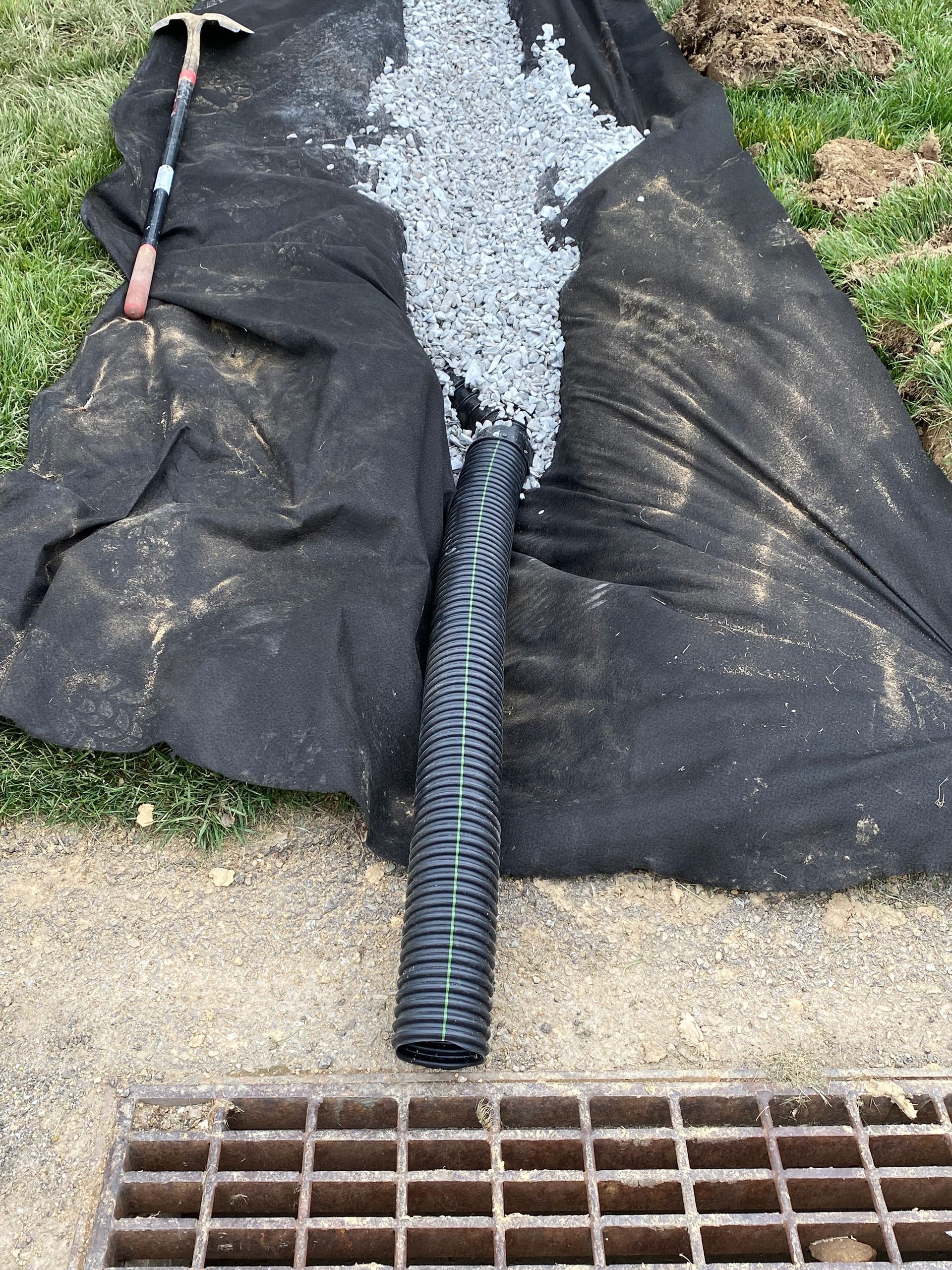 A black pipe is laying on top of a black tarp next to a drain.
