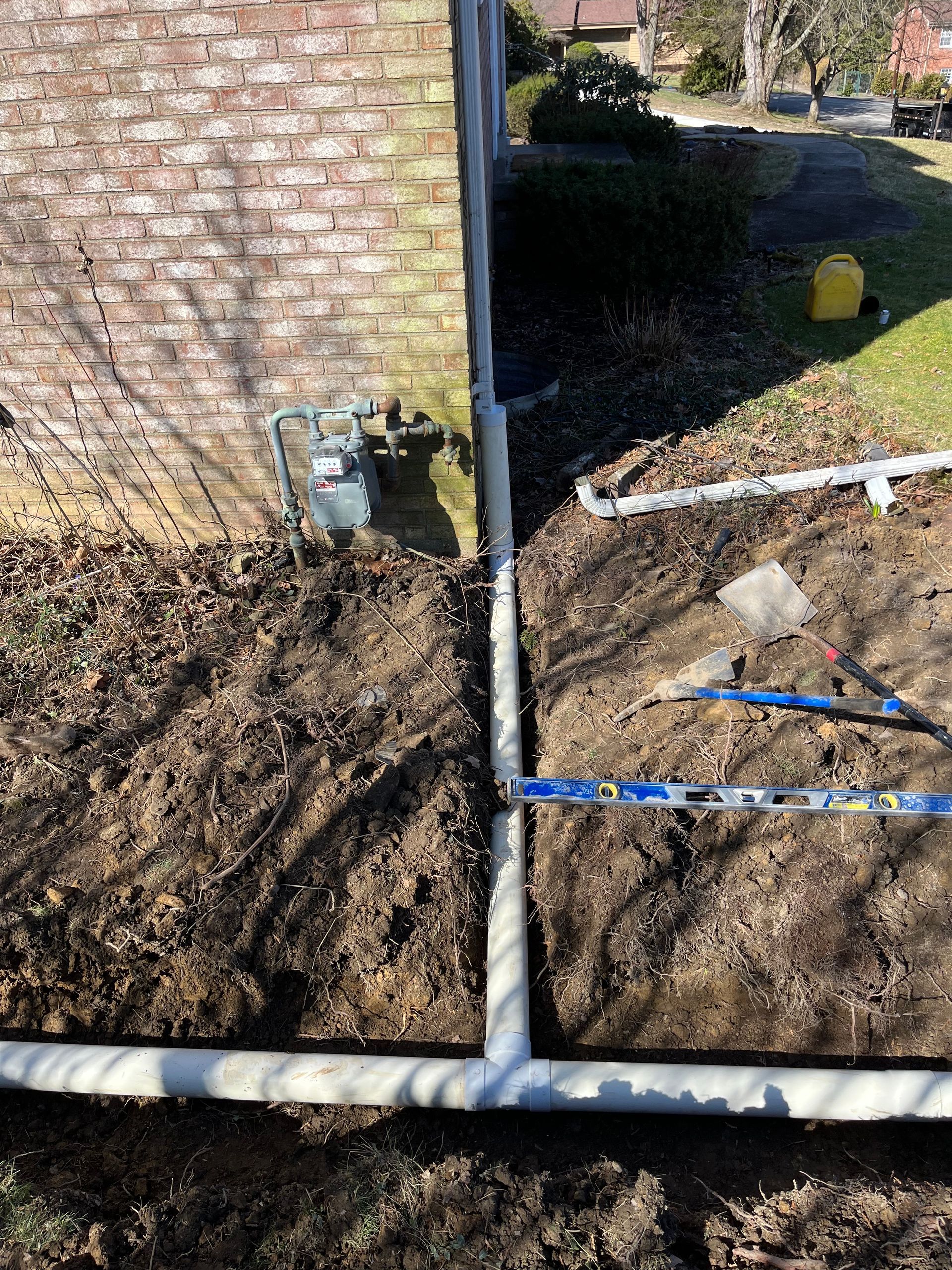 A pipe is being installed in the dirt next to a brick wall.