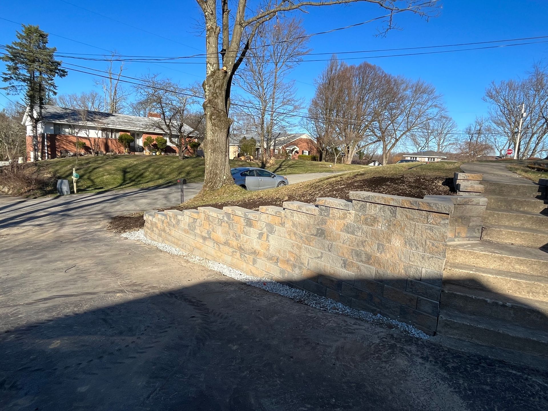 A stone wall is sitting on the side of a road next to a tree.