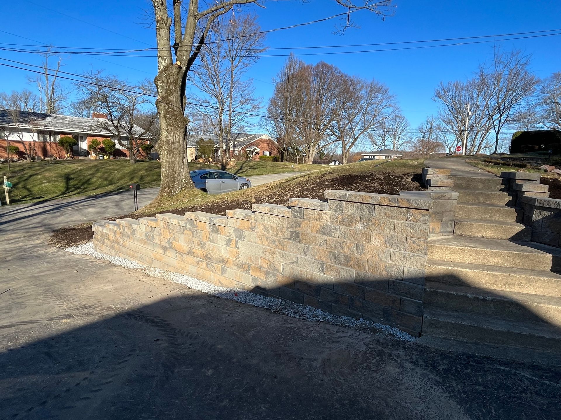 A car is parked on the side of the road next to a stone wall.