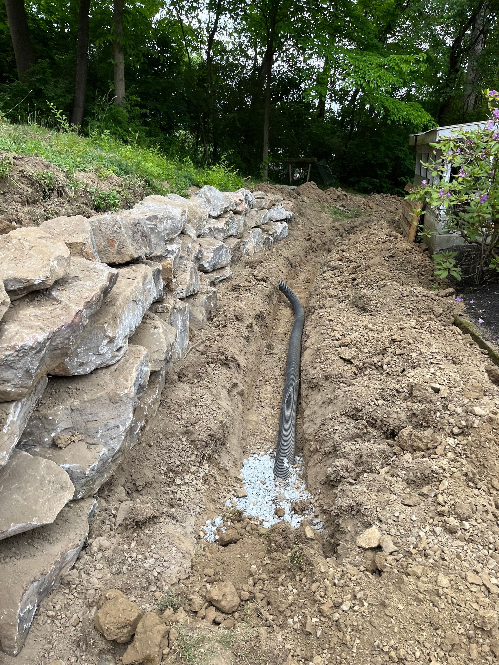 A hose is laying in the dirt next to a rock wall.