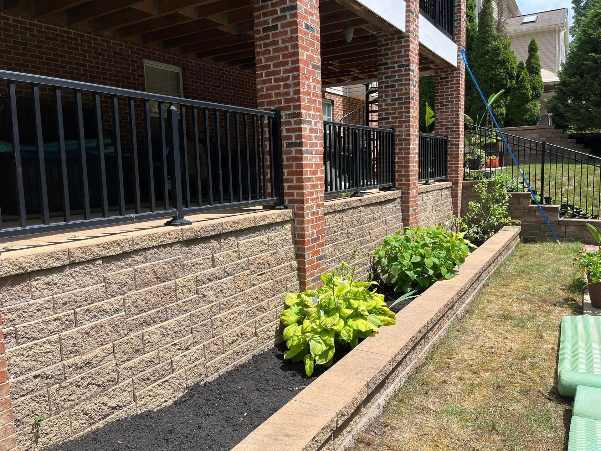 A brick wall with a fence and plants in front of a house.