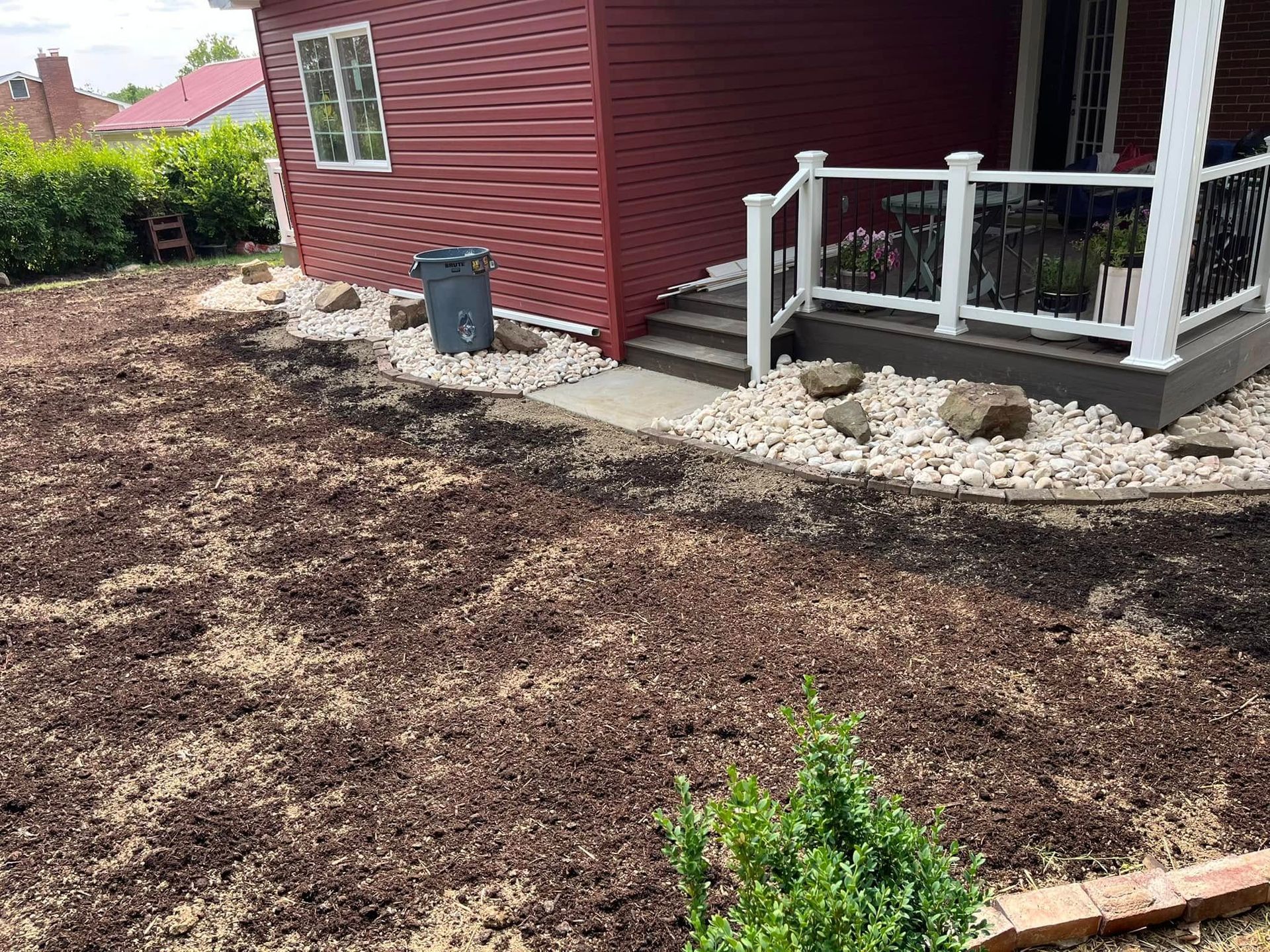 A red house with a white porch and a lot of dirt in front of it.