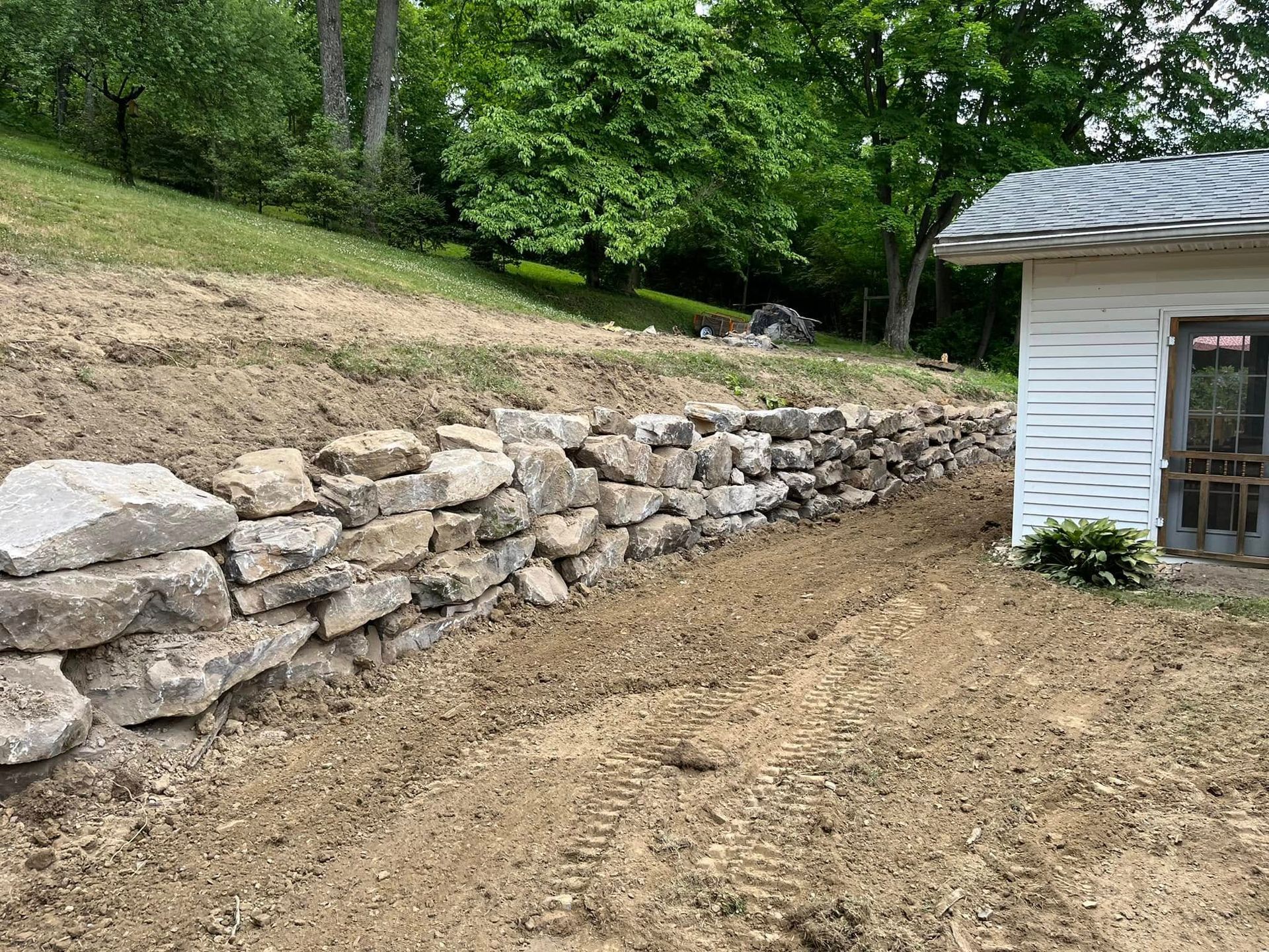 A stone wall is being built in the backyard of a house.