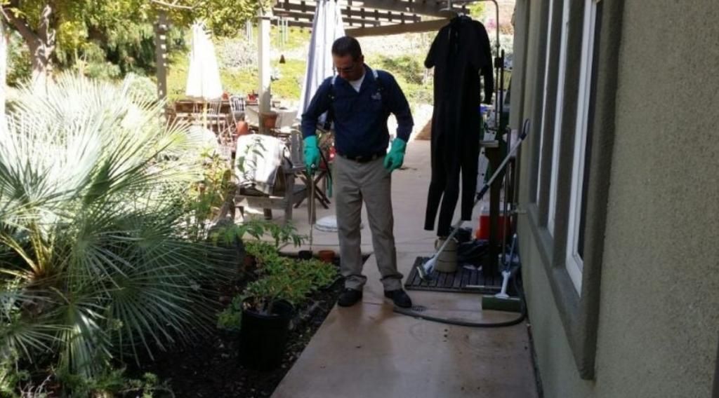 A man wearing gloves is standing on a sidewalk next to a house.