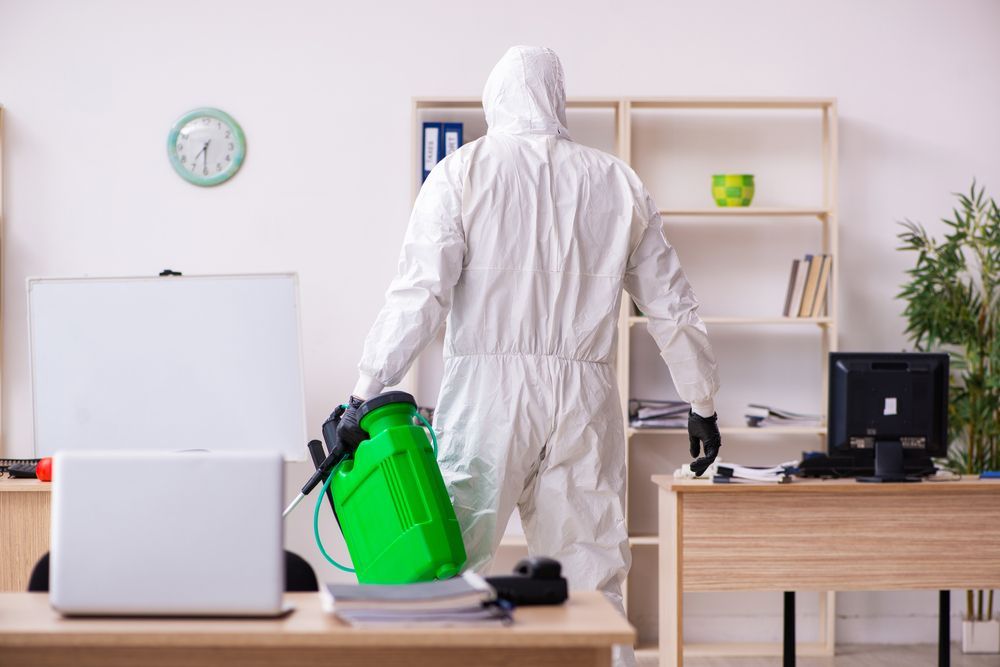 A man in a protective suit is disinfecting an office.