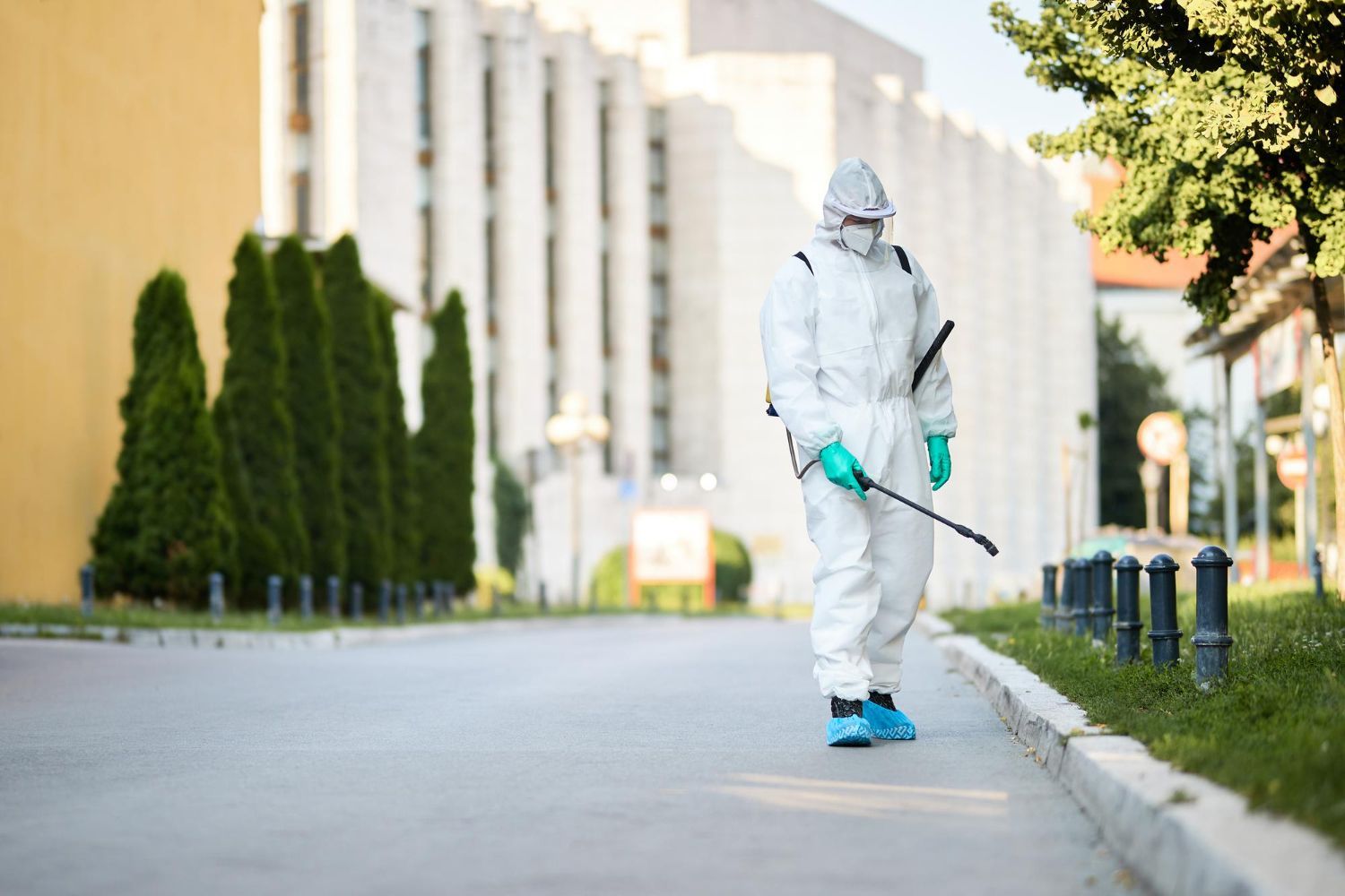 A man in a protective suit is spraying a street with a sprayer.