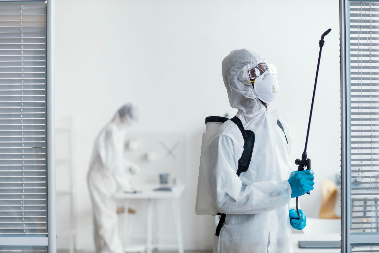 A man in a protective suit is spraying a room with a sprayer.