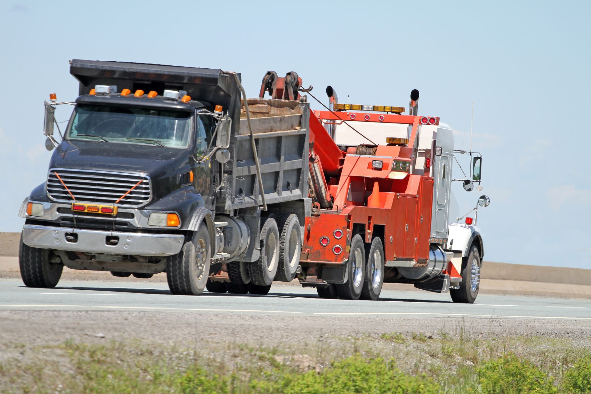 Tow truck towing a black dump truck on a highway.