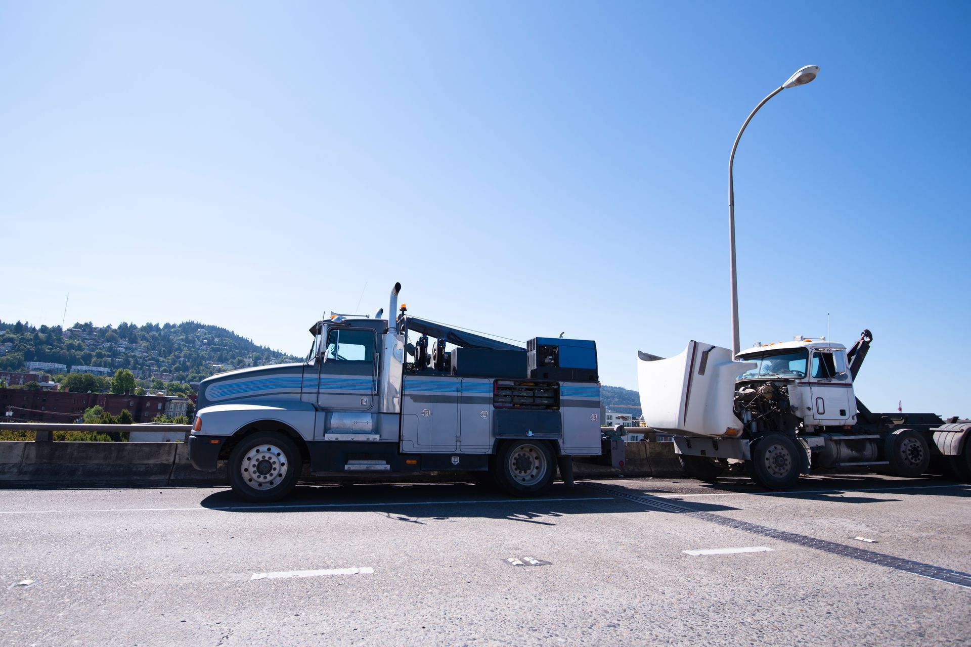 Two semi-trucks on a bridge, one blue, one white, with damaged trailers; blue sky background. Two semi-trucks on a bridge, one blue, one white, with damaged trailers; blue sky background.