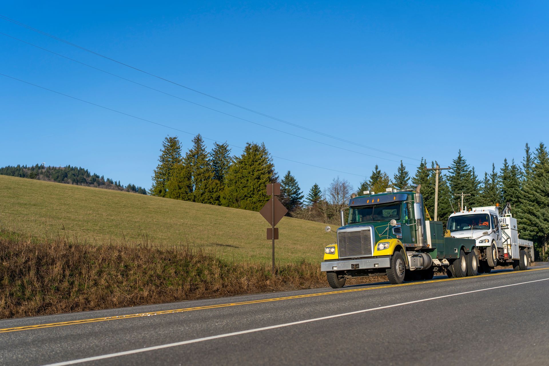 Semi-truck and trailer parked on a road, grassy hill in the background, clear blue sky.
