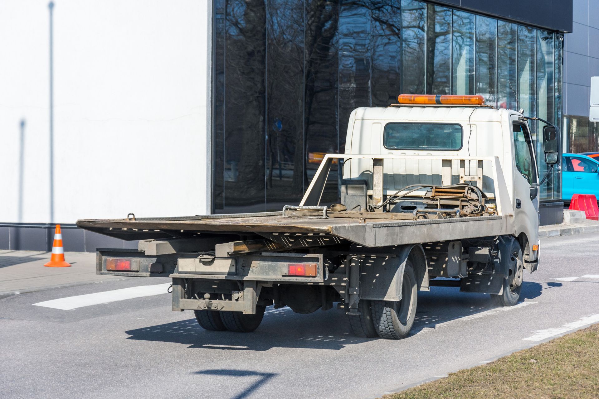 Tow truck on a road, preparing to load a vehicle, with a building in the background.