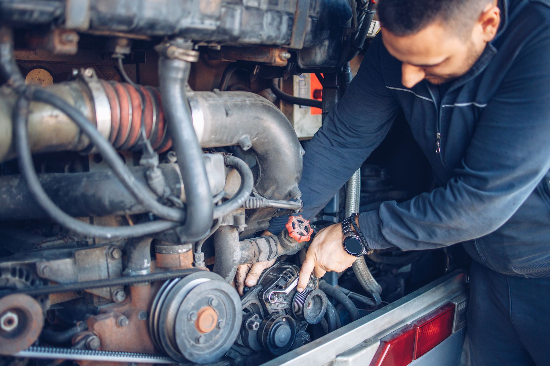 Mechanic working on an engine, pointing at a part. The setting appears to be a bus or large vehicle.