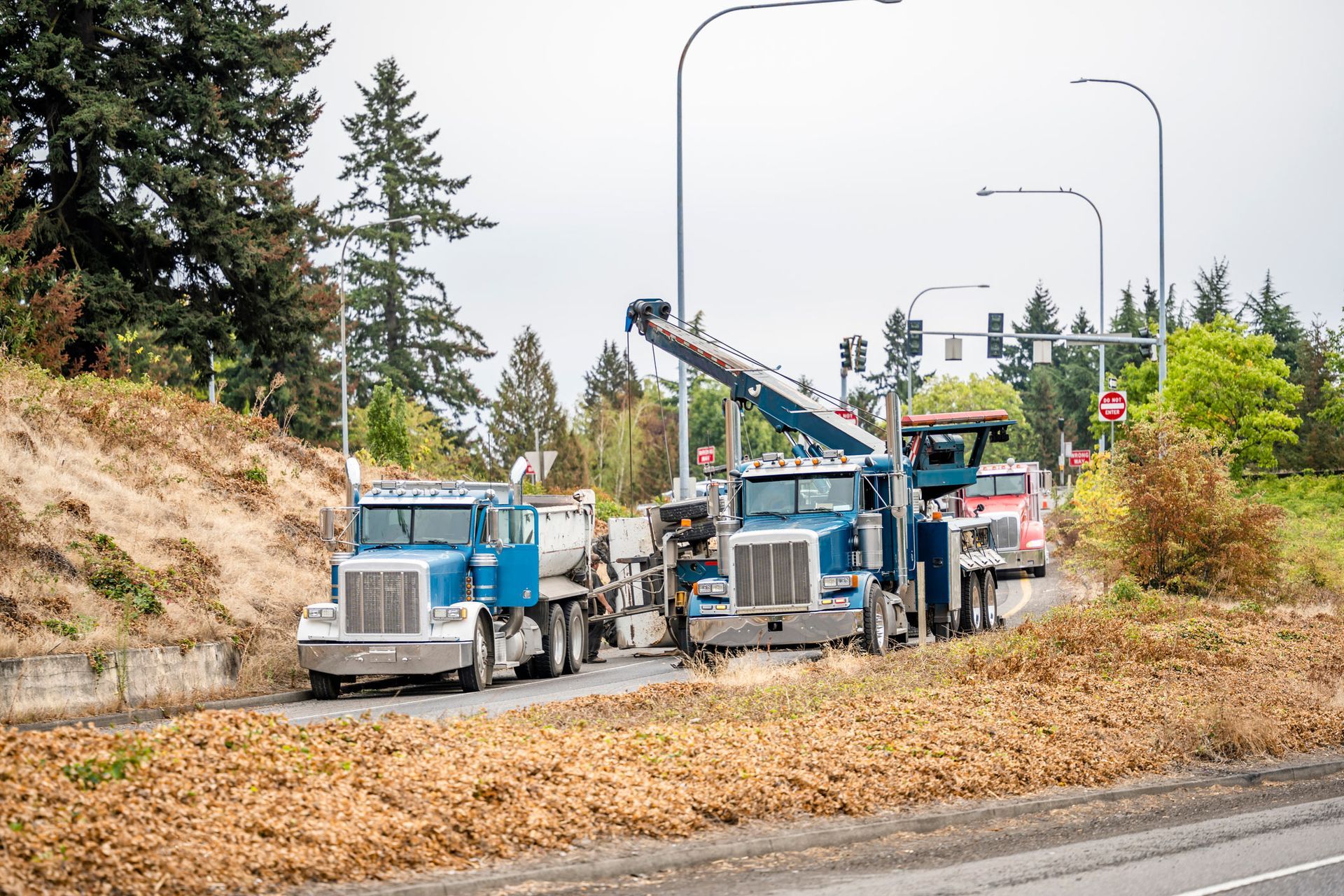 Two blue tow trucks on the side of a road, one lifting a vehicle. Trees and greenery in the background. Two blue tow trucks on the side of a road, one lifting a vehicle. Trees and greenery in the background.