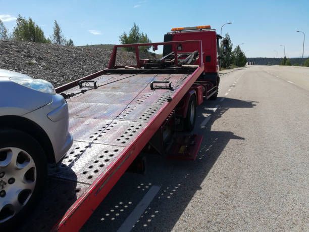 A silver car being towed by a red tow truck on a sunny roadside.