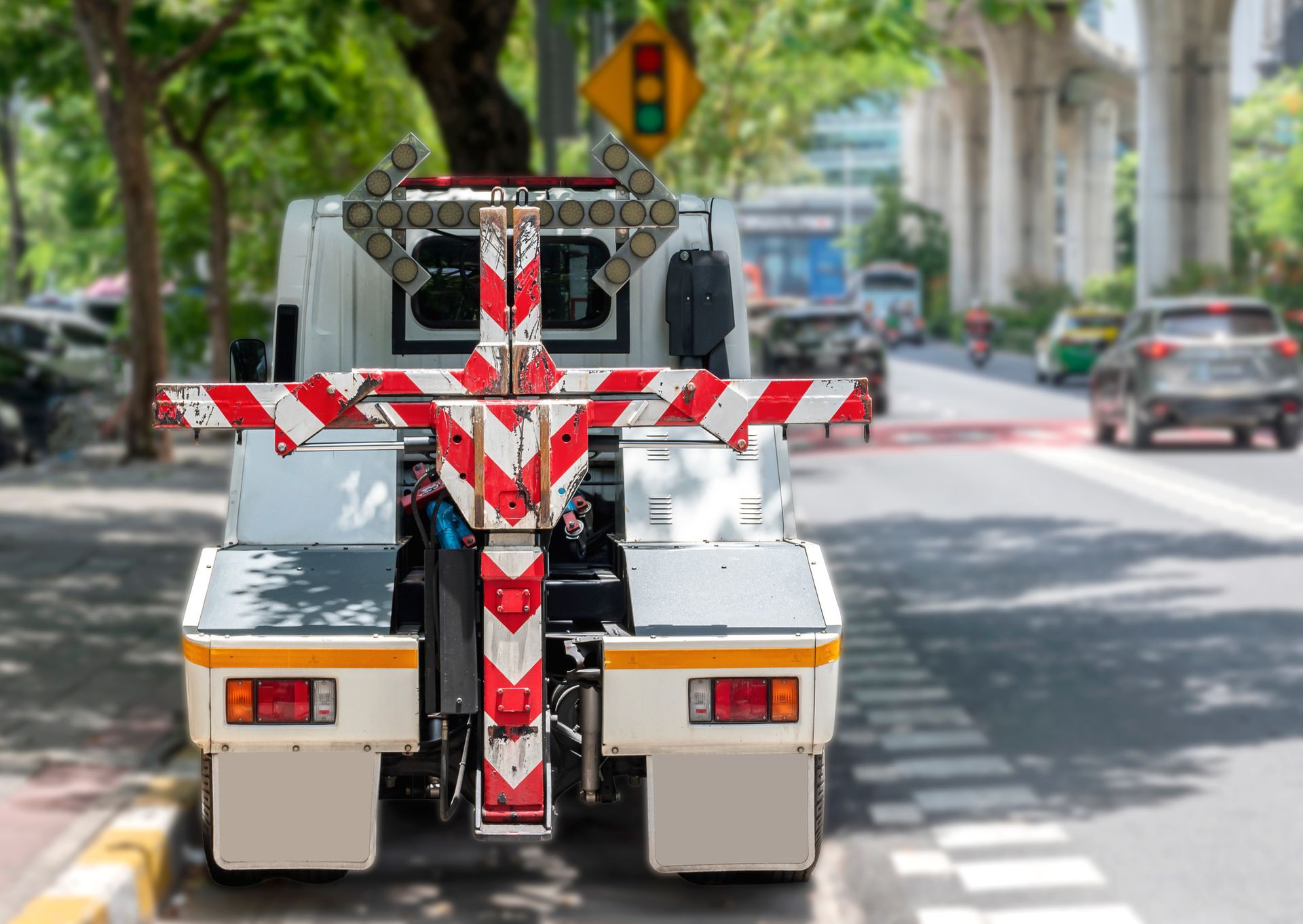 Tow truck on a city street with white and red striped equipment, traffic in background.