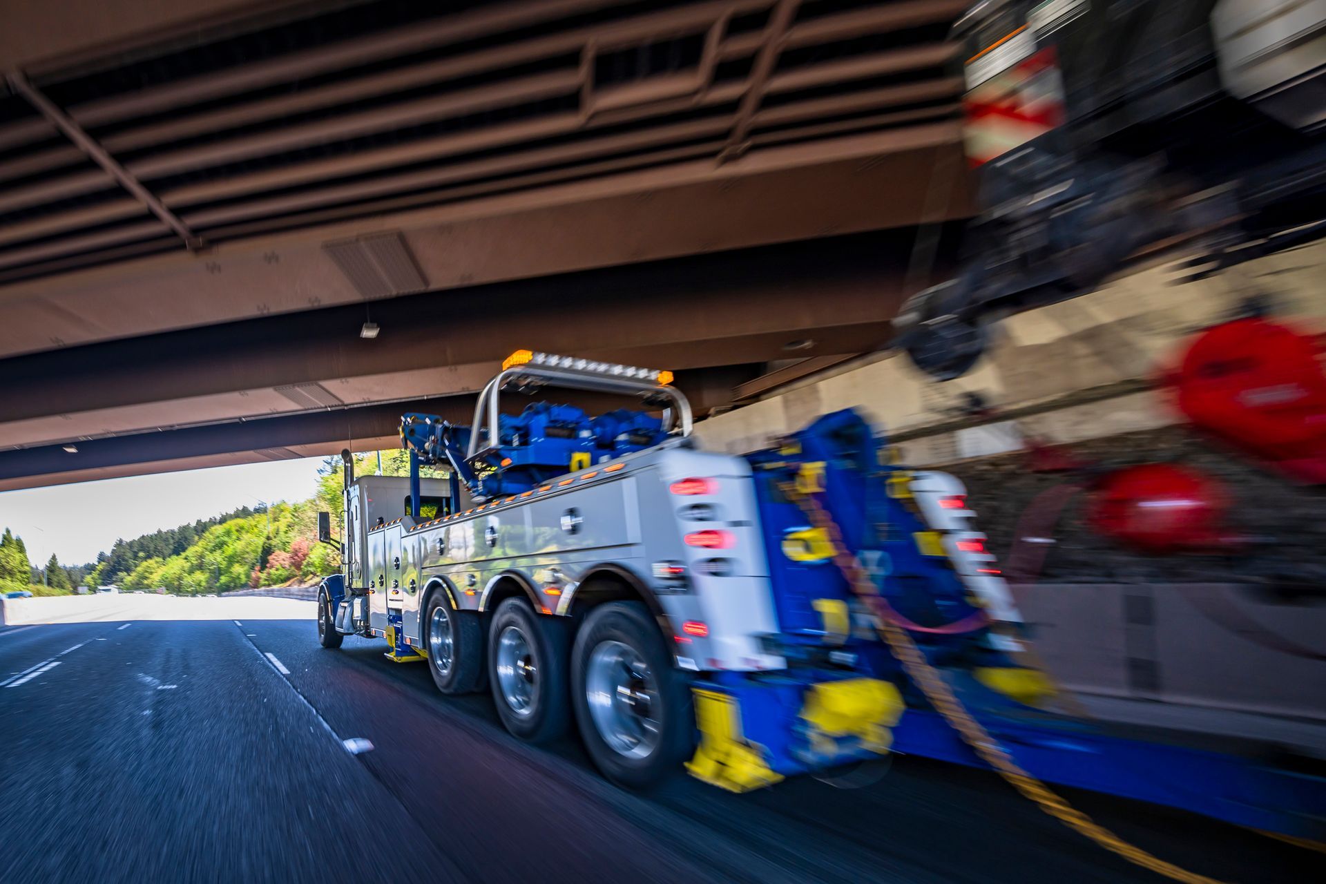 Tow truck towing a car on a highway, seen from a low angle under a bridge. Tow truck towing a car on a highway, seen from a low angle under a bridge.
