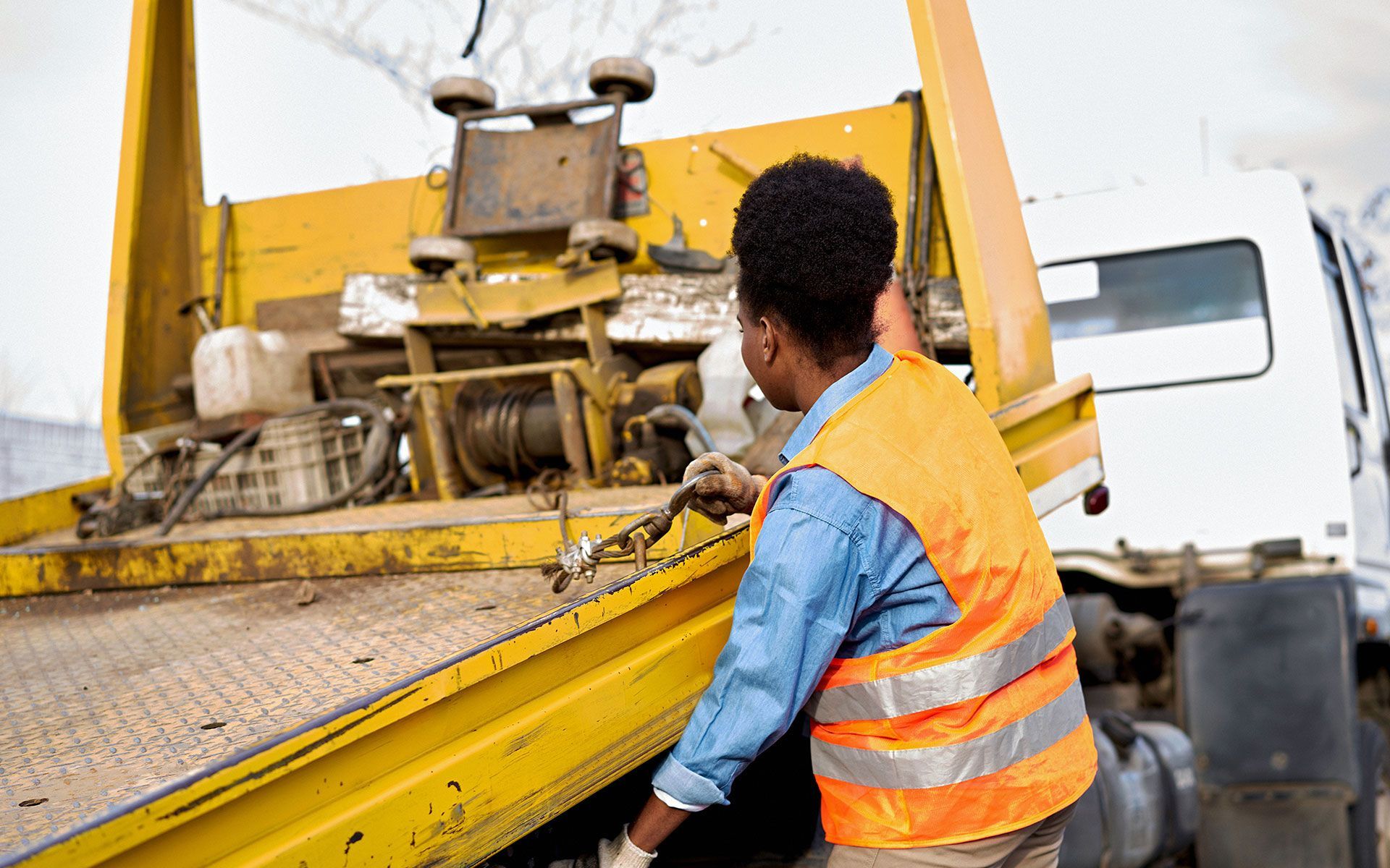 Woman in safety vest loading a vehicle onto a yellow tow truck.