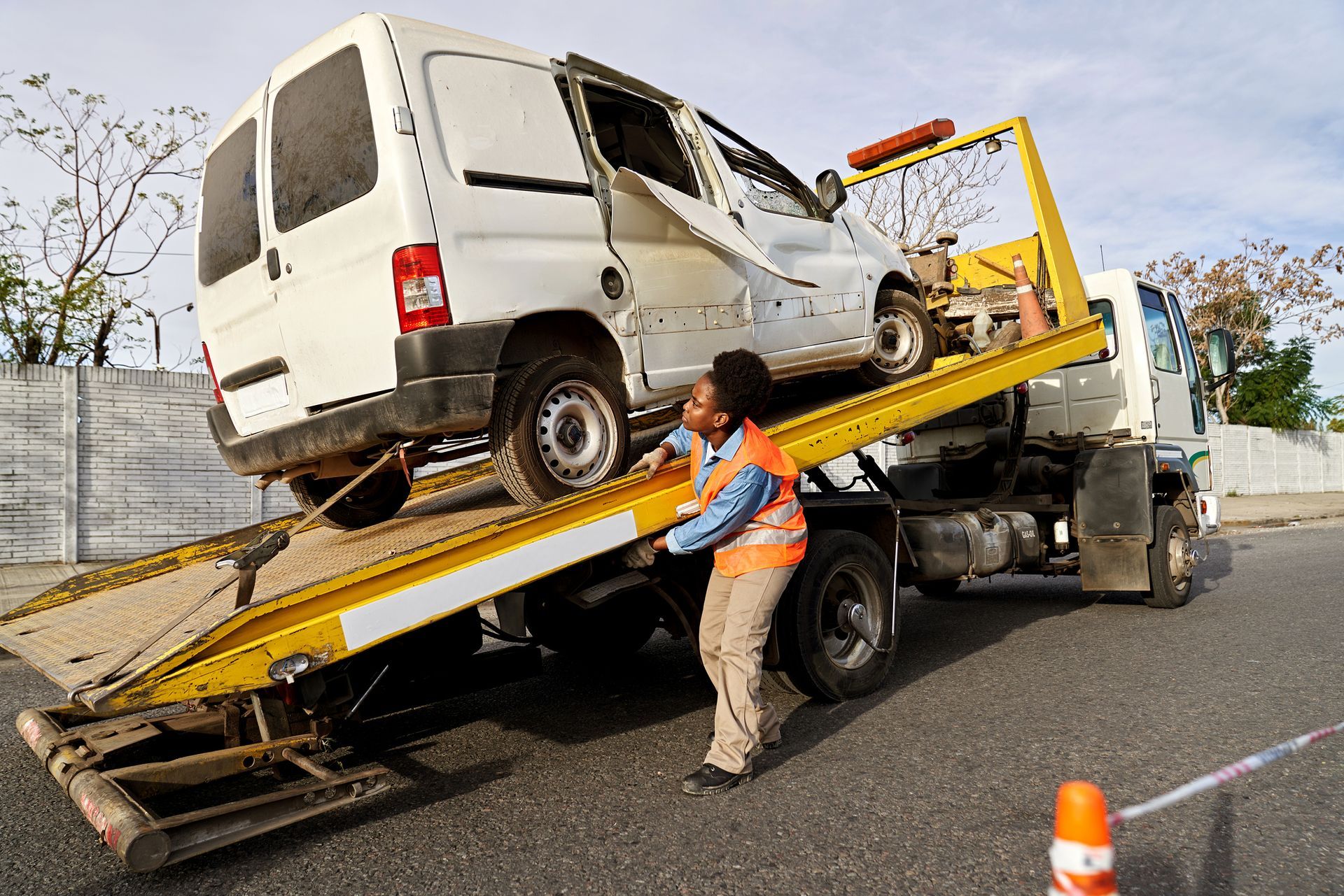 A tow truck operator loading a damaged white van onto a flatbed in a city street.