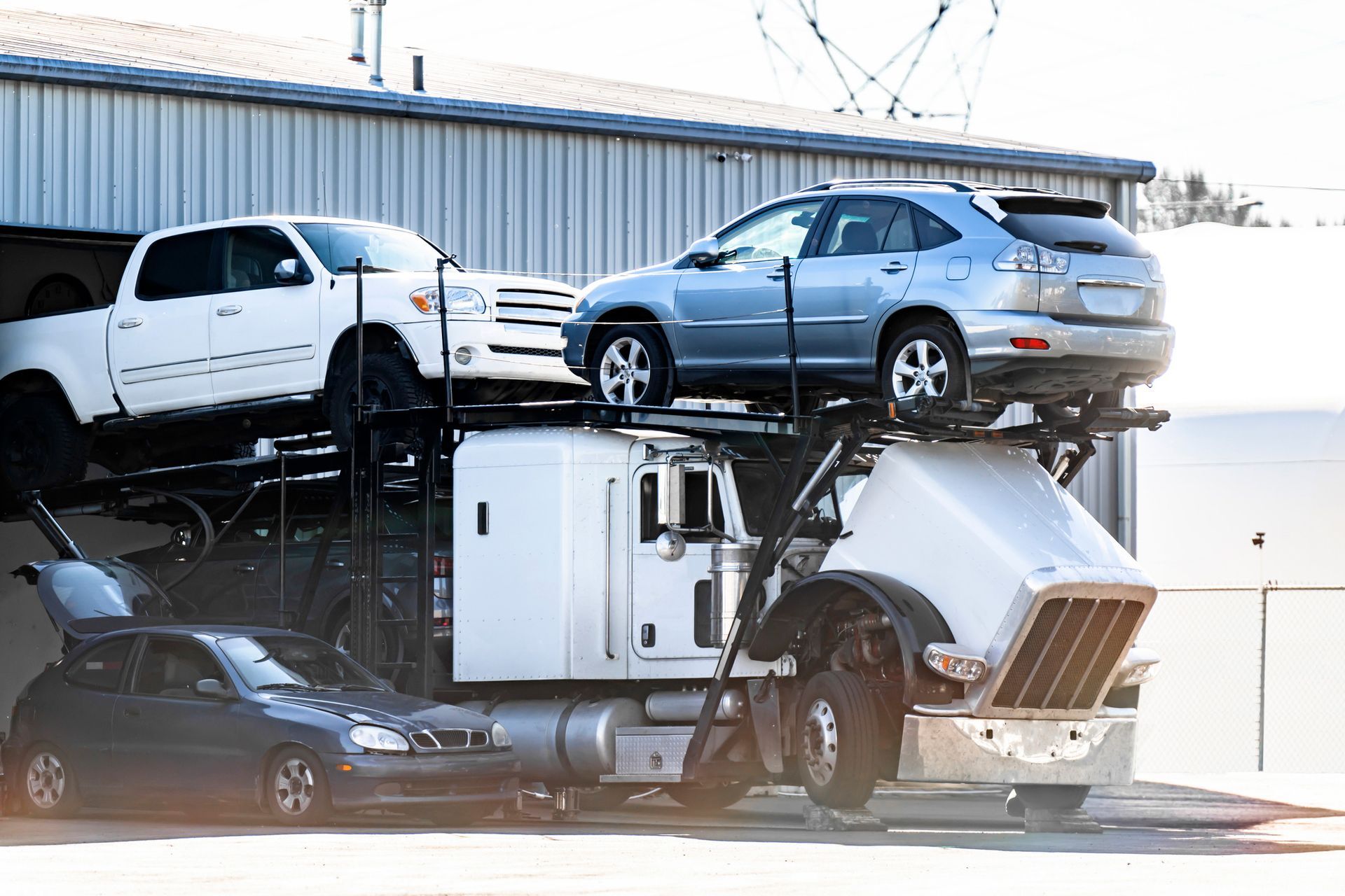 A car carrier truck with several vehicles loaded, parked next to a building.