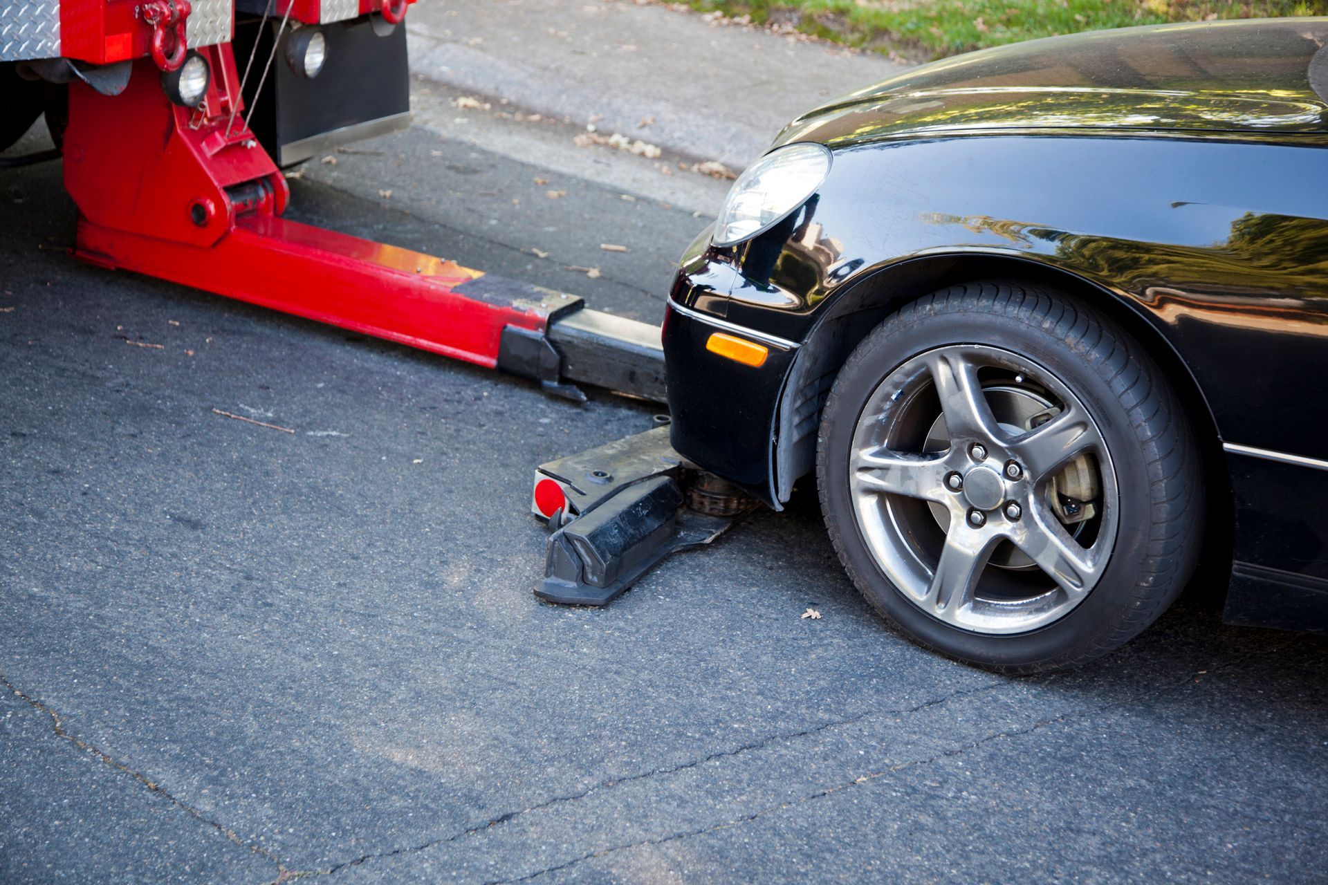 Black car being towed by a red tow truck on a street.