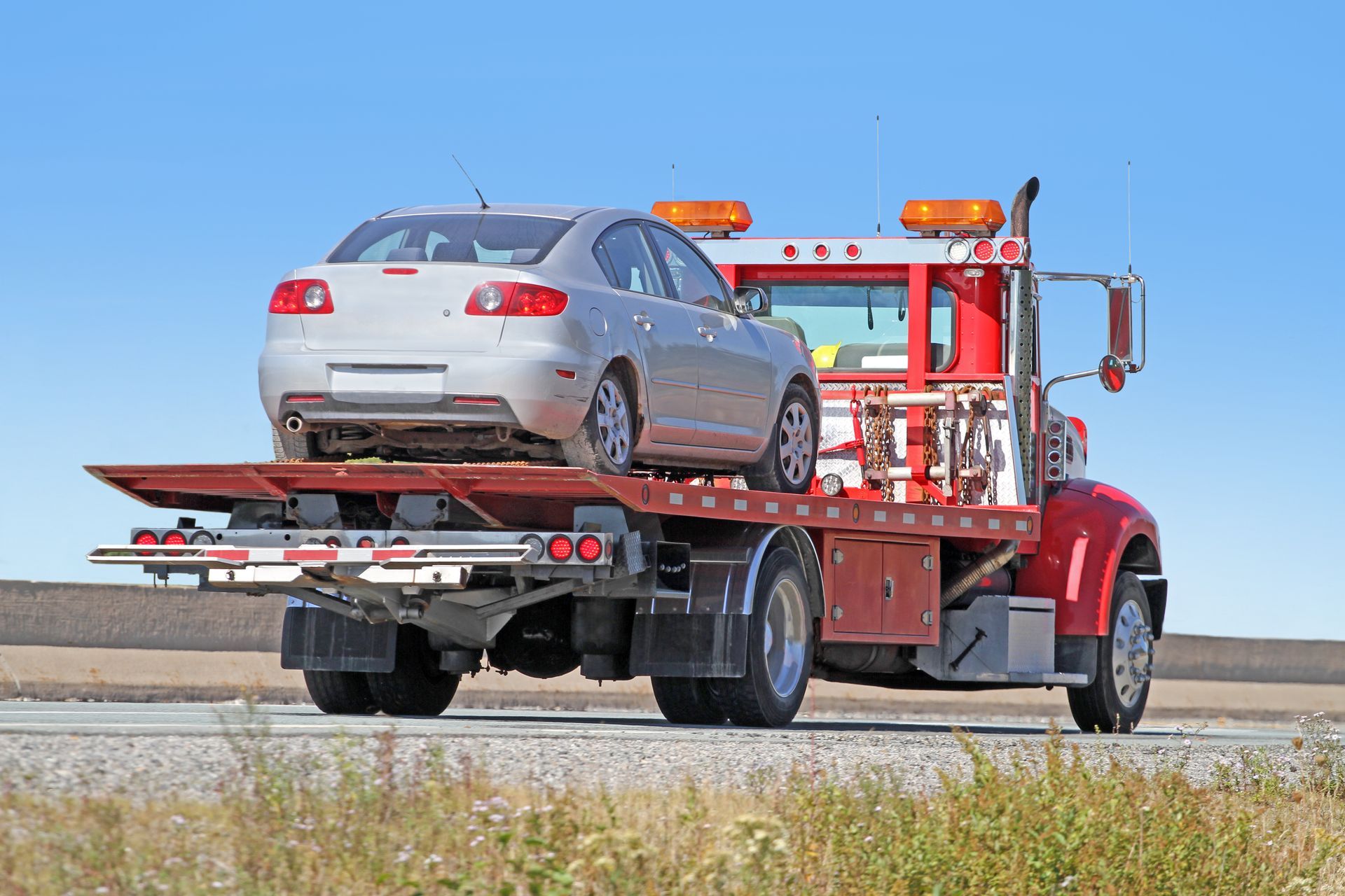 Silver car being towed by a red tow truck on a sunny road.