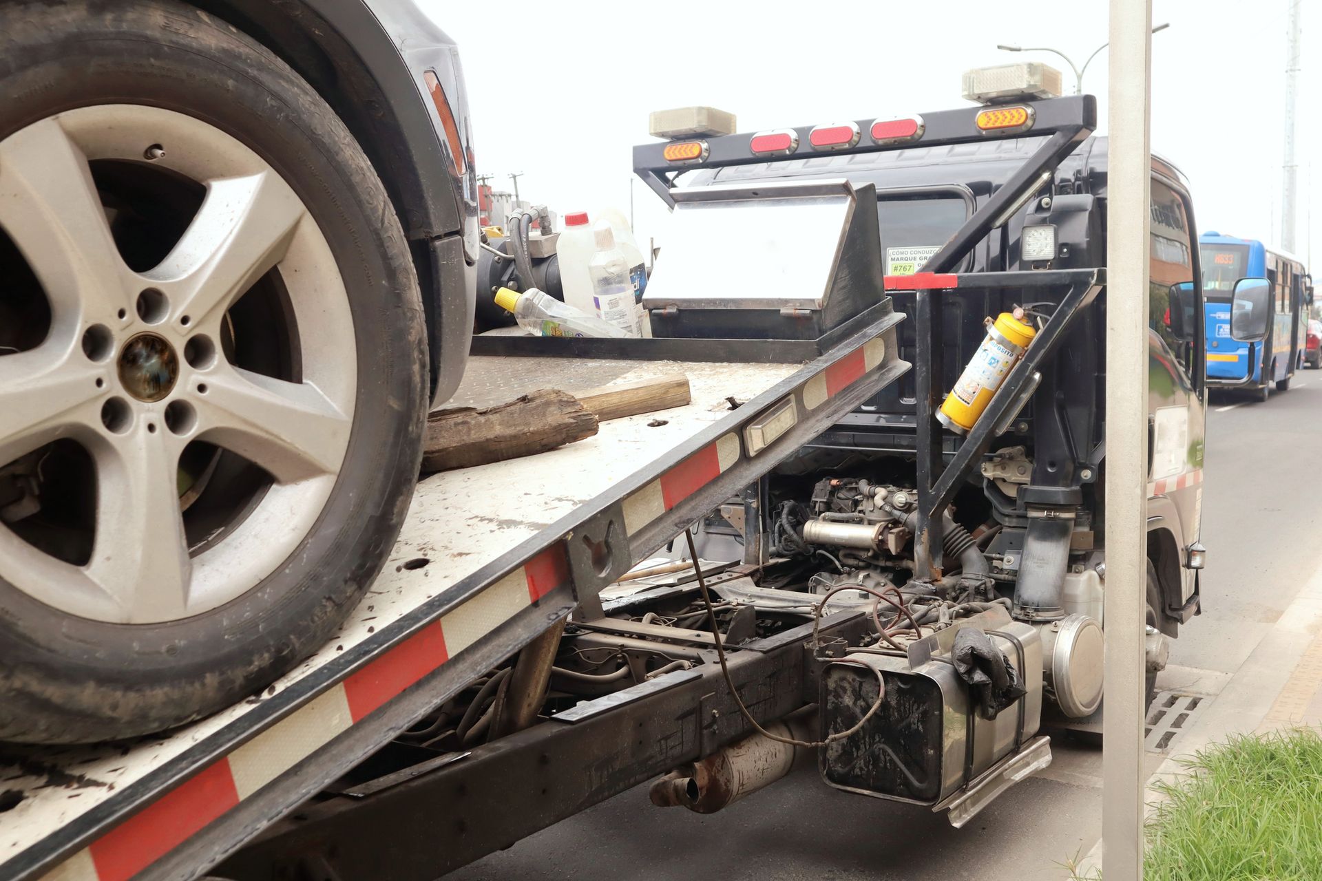 A black car on a tow truck. The car's tire is visible. A busy street and other vehicles are in the background.