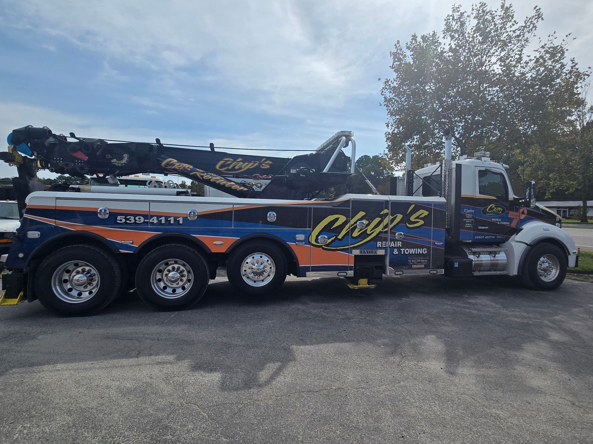 Tow truck with a black car on its flatbed, parked on a brick lot near a building.