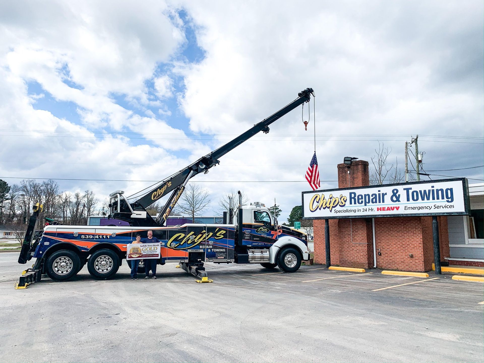 Tow truck uprighting a tipped over semi-truck cargo trailer on an overpass; two figures in dark coats walk nearby.