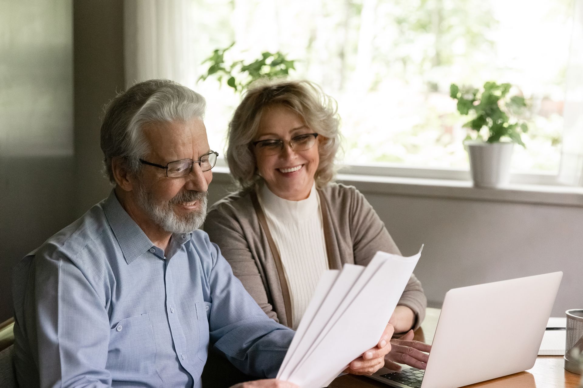 An Elderly Couple is Sitting at a Table Looking at Papers and a Laptop
