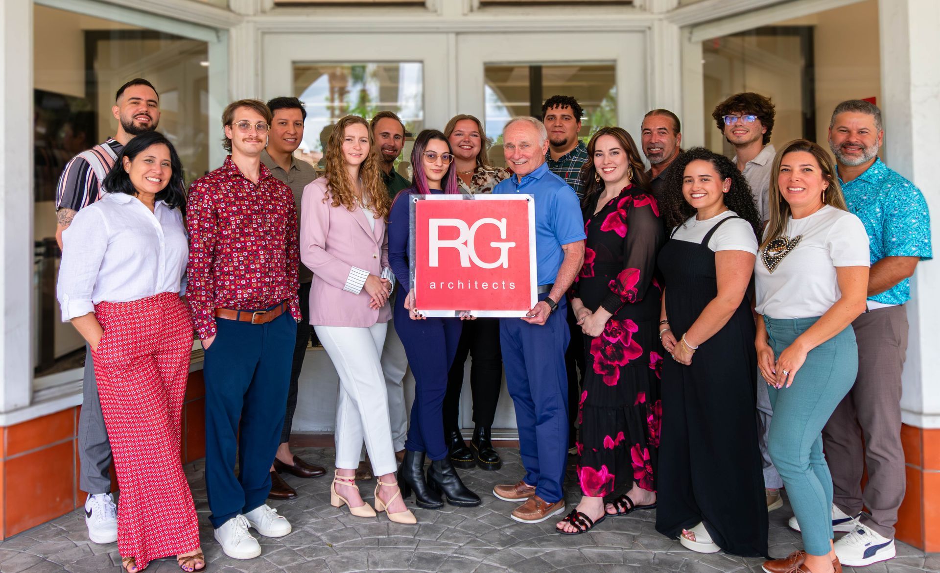 Group of people standing together indoors, smiling and holding a red RG sign in front of a doorway.