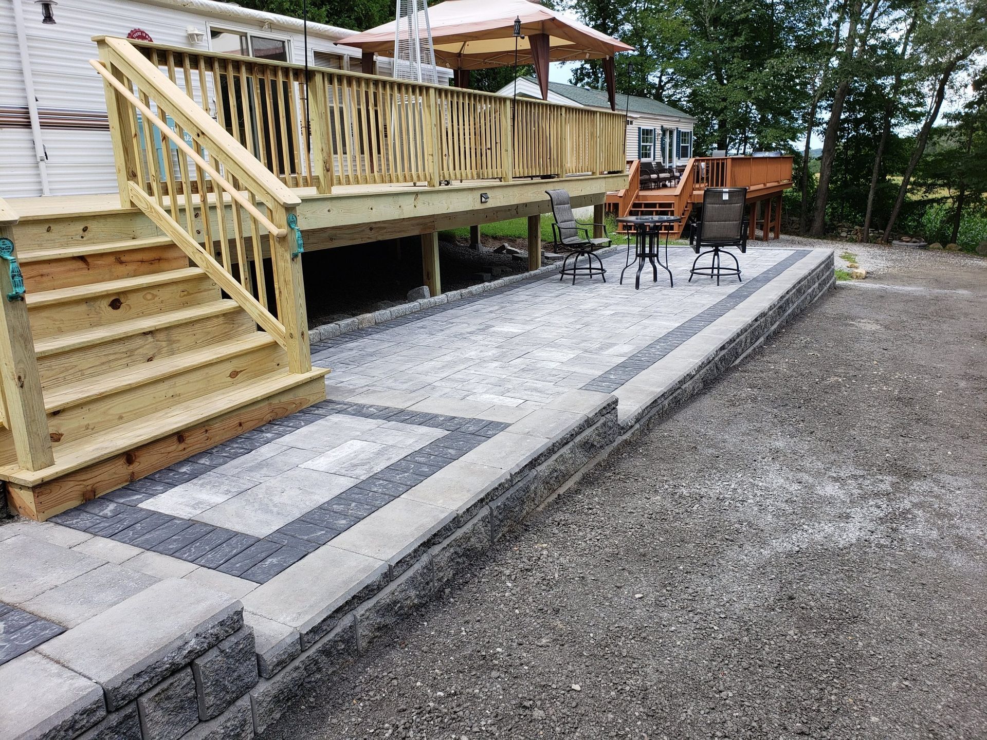 A wooden deck with stairs and a patio in front of a house.