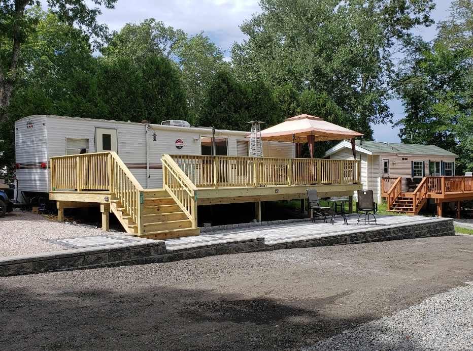 A rv with a large deck and stairs is parked in front of a house.