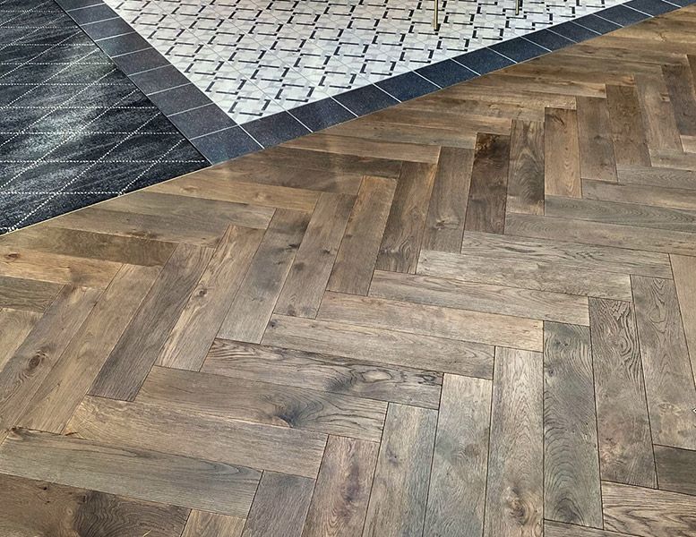 A Close-up Of a Wooden Floor with A Herringbone Pattern — Tony Di Milia Flooring in Unanderra, NSW