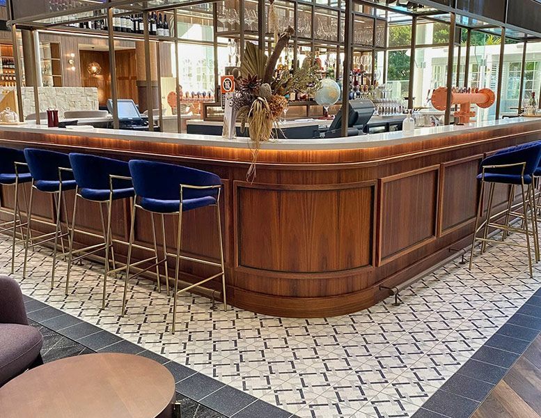 A Large Wooden Bar with Blue Chairs in A Restaurant — Tony Di Milia Flooring in Unanderra, NSW