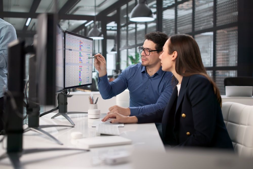 Two coworkers reviewing data on a large monitor in a modern office