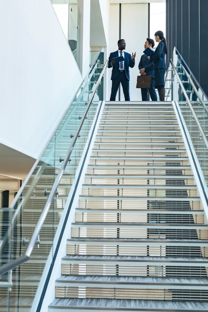 Businesspeople on a staircase, discussing plans in a modern office setting.