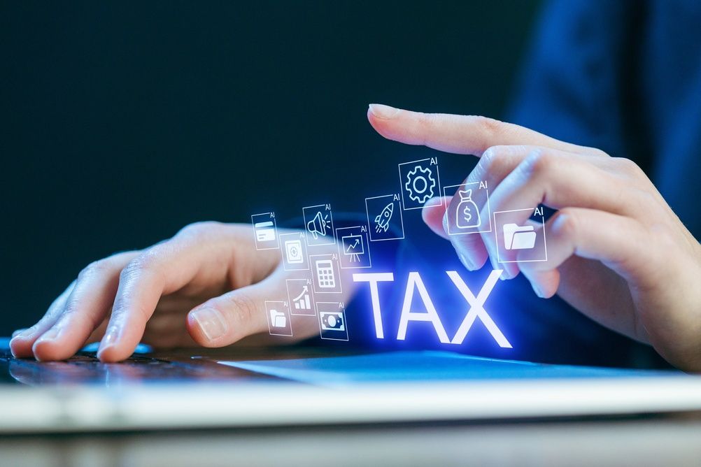 Hands typing on a laptop with glowing “TAX” text and digital finance icons above the keyboard.