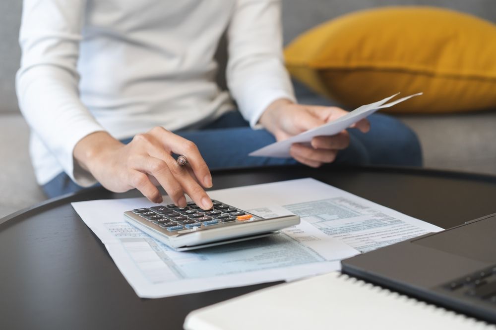 A woman is sitting at a table using a calculator and holding a piece of paper.