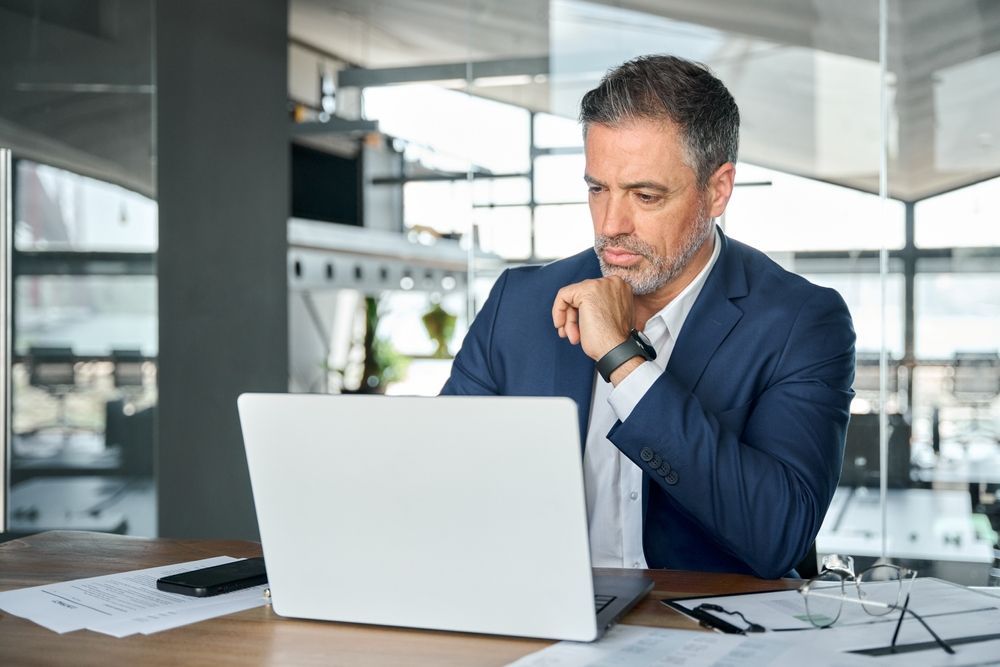 A man in a suit is sitting at a desk using a laptop computer.