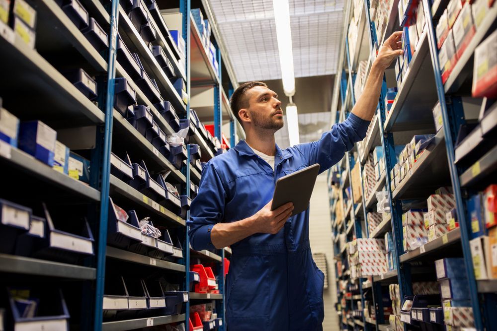 A man is standing in a warehouse looking at a tablet.