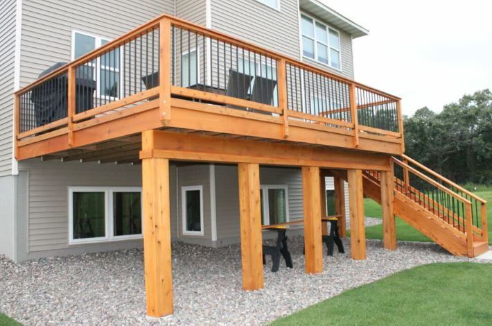 A large wooden deck with stairs leading up to it is in front of a house.
