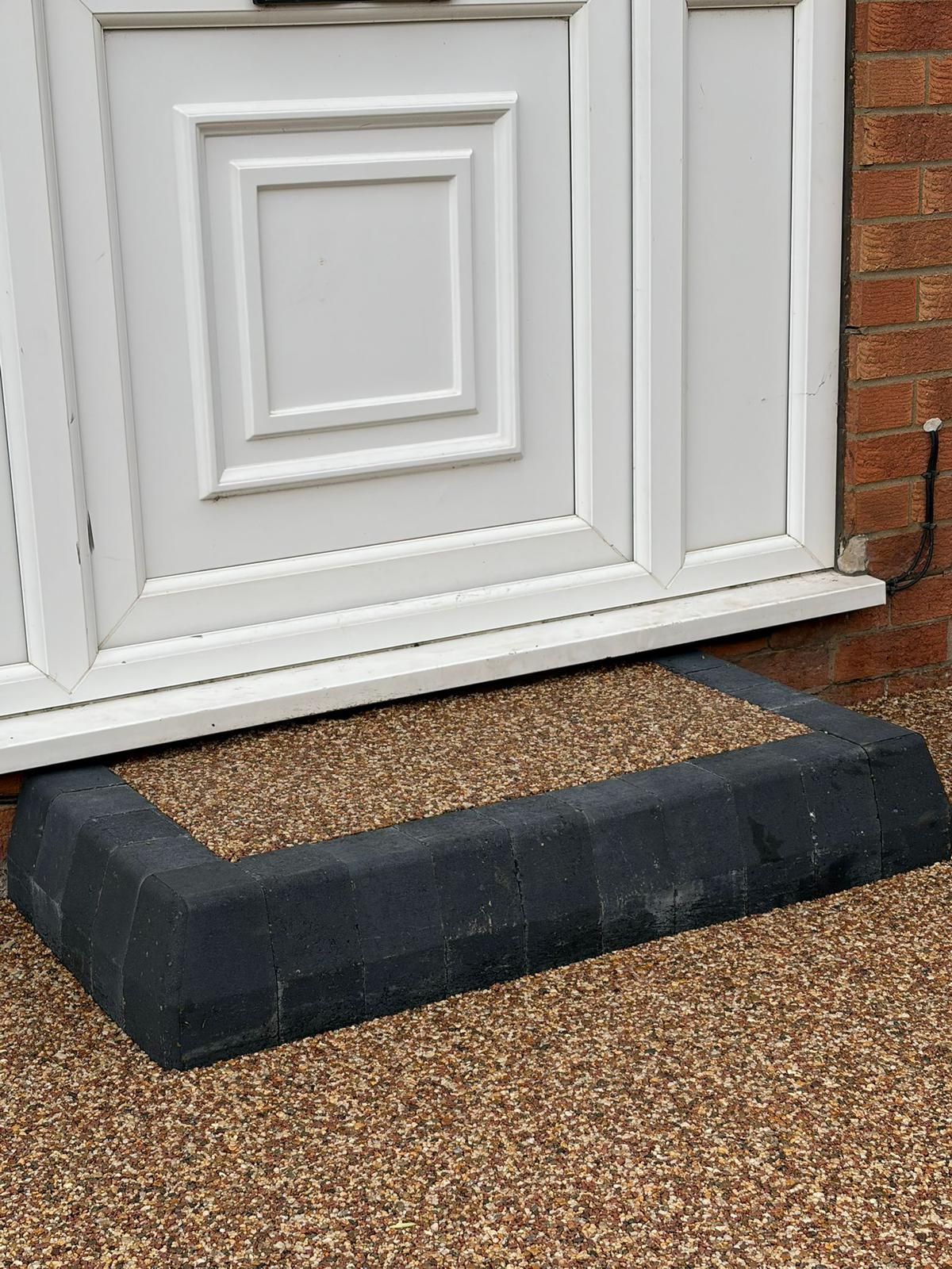 A white front door above a short step bordered by dark grey blocks and filled with loose light-brown gravel.