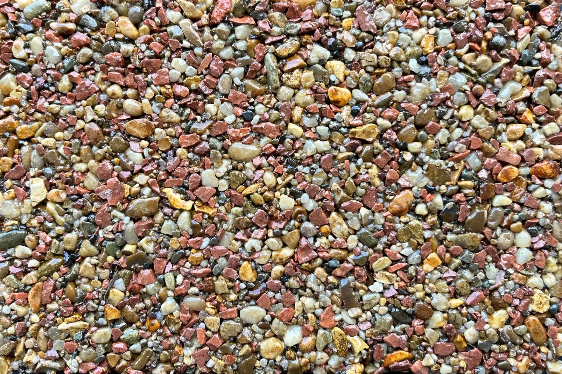 A close-up view of small, multicolored pebbles in shades of brown, red, gray, and cream packed tightly together.
