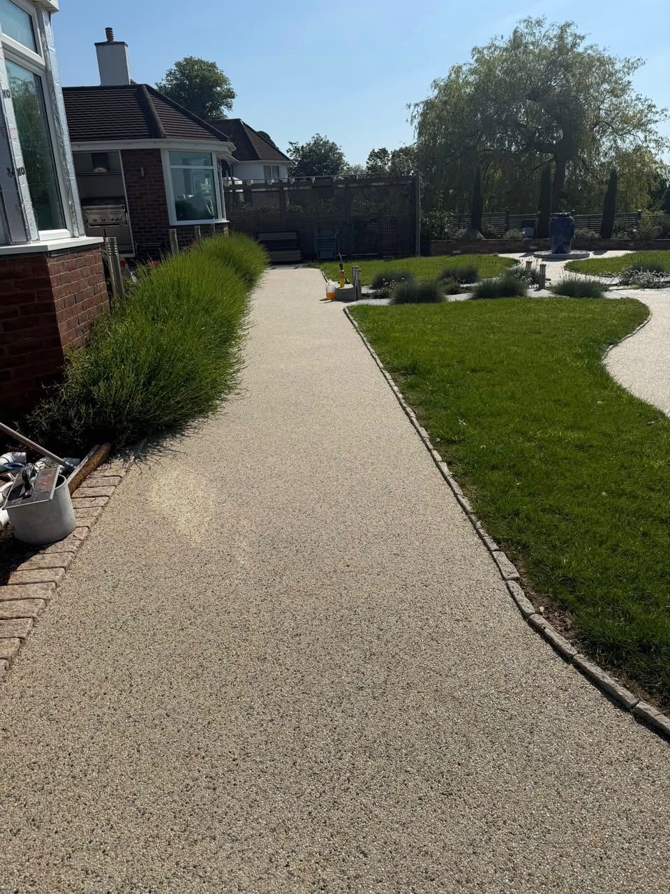Gravel walkway beside a house, bordered by hedges and lawn in a sunny garden.