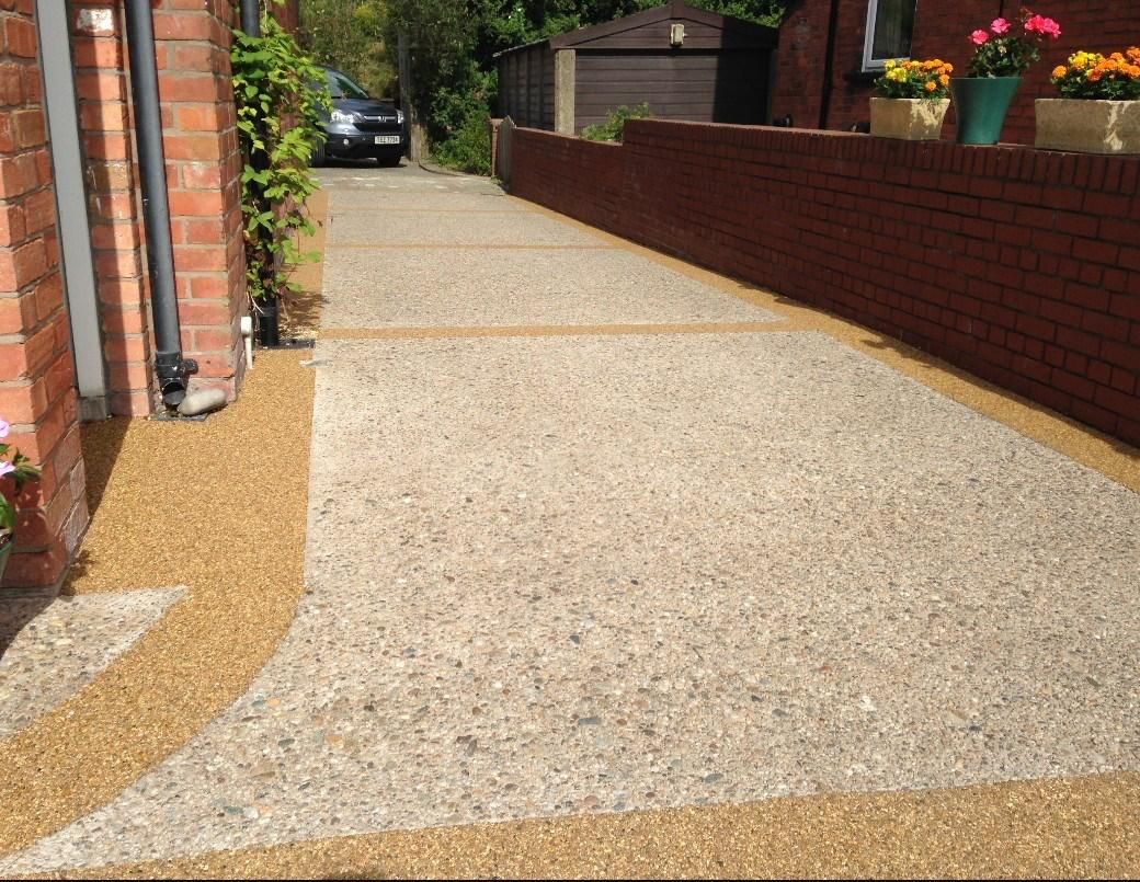 A walkway leading to a brick building with flowers in pots on the side.