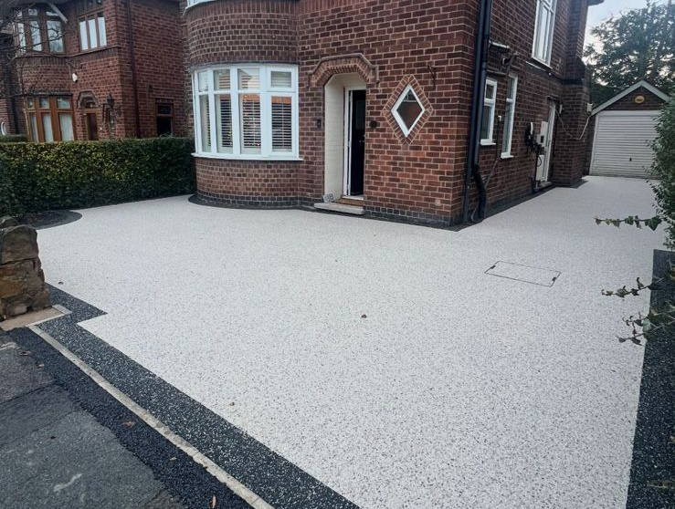 A red brick house with a newly installed white resin driveway featuring a dark grey border.