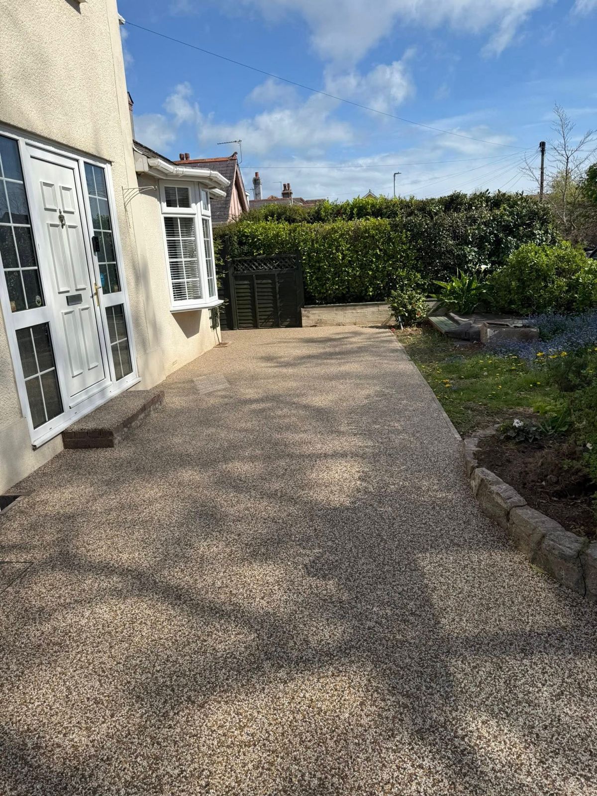 A newly laid light grey patio made of rectangular stone tiles, extending from the rear of a brick house into a garden.