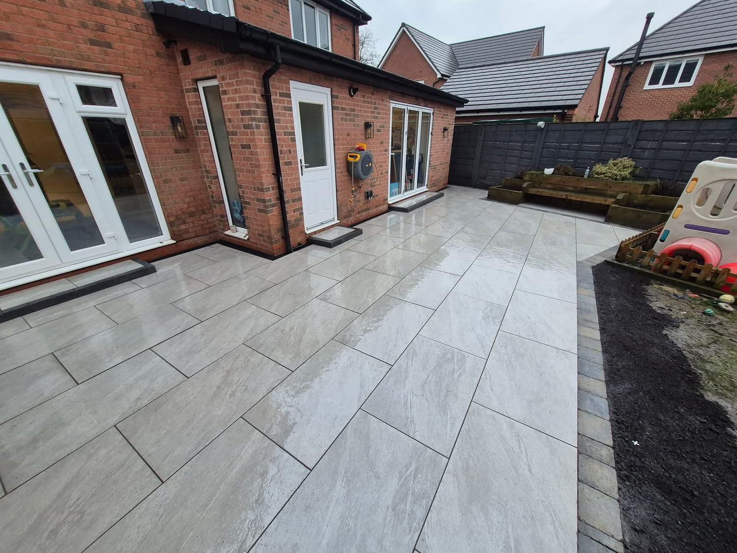 A modern two-story home with a white exterior, gray roof, and a large, newly paved gray resin driveway.